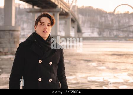 Portrait of teenage boy wearing coat and scarf while standing by river in winter Stock Photo