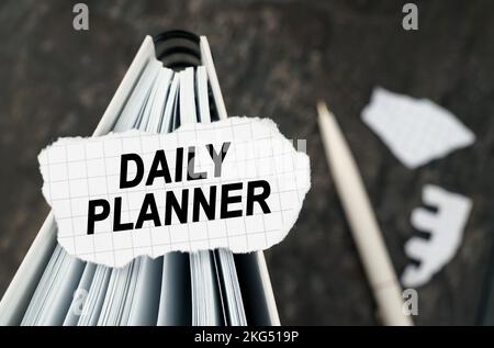 On the table is a notebook on which lies a piece of torn paper with the inscription - Daily planner. The pen lies outside the sharpness zone. Stock Photo