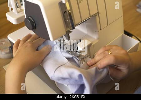 A woman designer works on an overlock sewing machine on tailoring. Close-up. Small tailoring business. Stock Photo