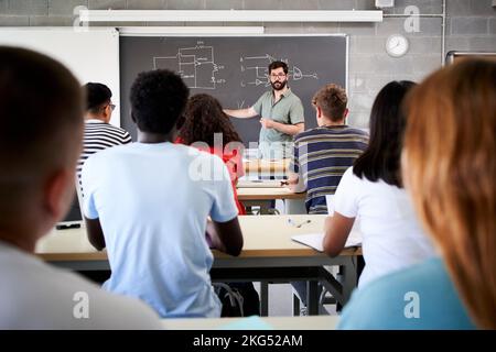 Male Tutor Teaching University Students In Classroom. Rear view from college attending at teacher in class. Professor explains the lesson on the Stock Photo