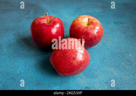 Three red apples lie on a blue background Stock Photo