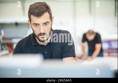 Professional worker printmaker technician operator works in printing press hall and printshop office with many different type of machine Stock Photo