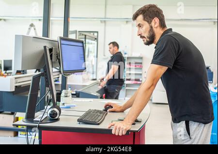 Professional worker printmaker technician operator works in printing press hall and printshop office with many different type of machine Stock Photo