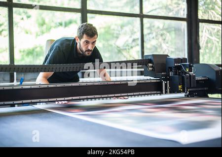 Professional worker printmaker technician operator works in printing press hall and printshop office with many different type of machine Stock Photo
