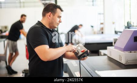 Professional worker printmaker technician operator works in printing press hall and printshop office with many different type of machine Stock Photo
