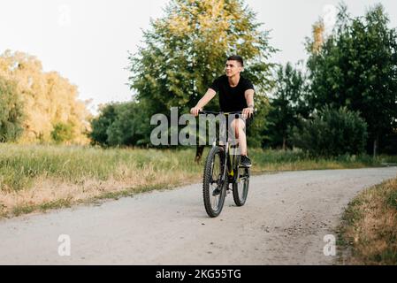 A man in black t-shirt rides a bicycle along a path in the park Stock Photo