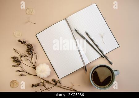 Notepad copyspace, gray pencils and cup of coffee on tan begie background with dry brown branches. Autumn minimal flatlay Stock Photo