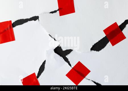 Ripped up pieces of white paper stuck together with red tape on black background Stock Photo