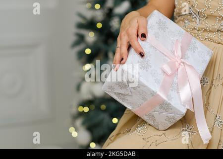 Closeup shot of female hands holding beautiful Christmas present with pink ribbon on white background in interior Stock Photo