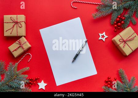 Creative design red background and branches of Christmas trees, gifts, candy canes and paper card note. Stock Photo