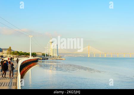 LISBON, PORTUGAL - NOVEMBER 11, 2021: People on promenade at sunset, Vasco da Gama bridge, Myriad hotel modern building in background Stock Photo