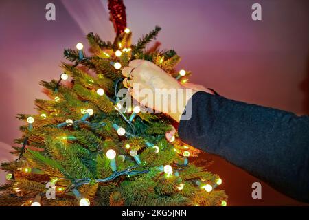 Womans hands with rings putty electric lights on artificial Christmas tree - closeup and selective focus Stock Photo