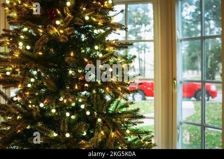Christmas in the South - Christmas tree with lights in front of a blurred bay window showing green grass and trees and a red pickup truck Stock Photo