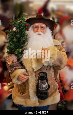 Cowboy Santa Claus in shearling coat with saddle and lantern and Christmas tree - selective focus - blurred background Stock Photo