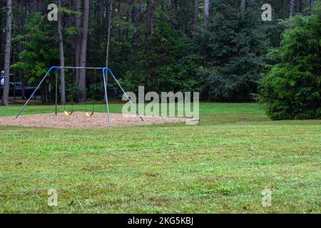 A swing set sits empty on a hot afternoon at the camp grounds in Arkansas. The lush green grass and tree lines park is peaceful and inviting. The chil Stock Photo