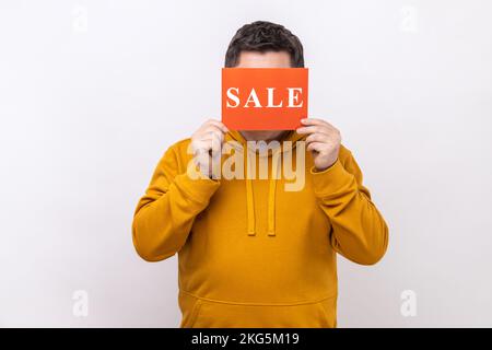 Portrait of unknown anonymous man covering eyes with Sale inscription, market discounts, black friday, wearing urban style hoodie. Indoor studio shot isolated on white background. Stock Photo