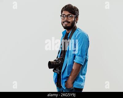 Professional photographer having DSLR camera taking picture.Indian man photography enthusiast taking photo while standing on blue background. Studio Stock Photo