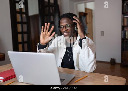 Smiling optimistic African American man waving hand having video call in laptop with friends Stock Photo