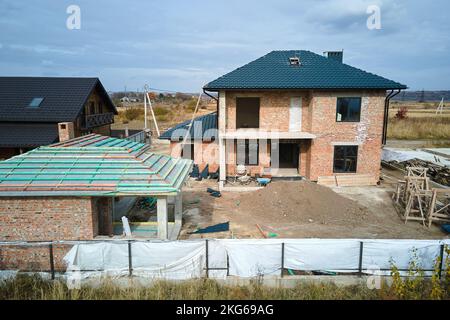 Aerial view of unfinished house with brick walls and wooden roof frame covered with metallic tiles under construction Stock Photo