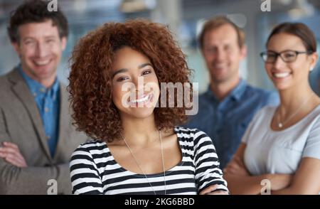 Theres a lot to smile about in my professional life. Portrait of a smiling young woman with friendly coworkers in the background. Stock Photo