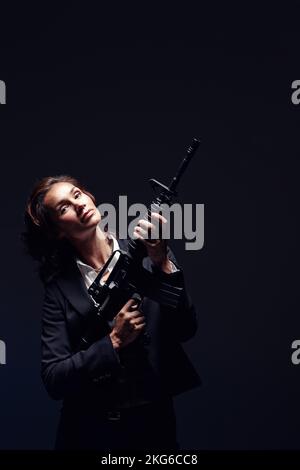 Powerful position. a mature woman wearing a suit and holding an automatic rifle. Stock Photo