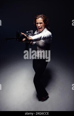 In the mood to shoot. Full length shot of an aggressive woman standing under a spotlight and pointing a rifle. Stock Photo