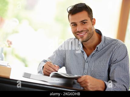 Hes the boss of his books. Portrait of a smiling young man studying from a book. Stock Photo