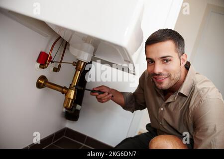 Hell work magic on your pipes. Portrait of an attractive young man fixing a pipe underneath the basin. Stock Photo