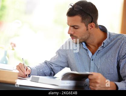 Its called continuing professional development...a young man writing notes from the book that hes studying. Stock Photo