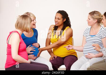 Shes a strong kicker. An African-American woman touching her pregnant friends belly while they sit in a group having a discussion. Stock Photo