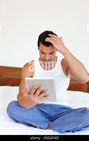 Getting to grips with new technology. A man sitting on his bed holding a digital tablet. Stock Photo