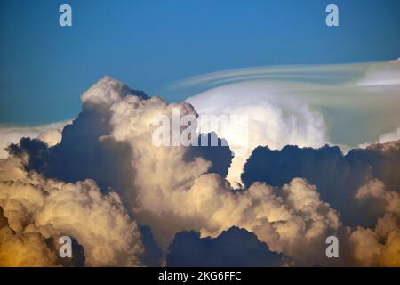 White fluffy cumulonimbus clouds forming before thunderstorm on evening sky. Changing stormy cloudscape weather at sunset Stock Photo