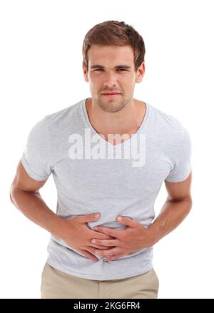 Maybe its time to cut out the take away menu. a young man holding his tummy in pain while standing in a studio-isolated on white. Stock Photo