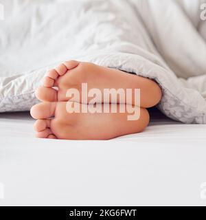 First stirring on a bright morning. a pair of feet poking out from under a blanket. Stock Photo