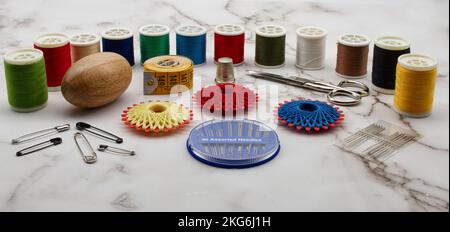 Sewing tools and accessories: scissors, tape measure, spools of thread, needle, thimble and pins isolated on marble background. Stock Photo