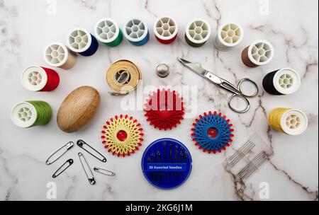 Sewing tools and accessories: scissors, tape measure, spools of thread, needle, thimble and pins isolated on marble background. Top view, flat lay Stock Photo