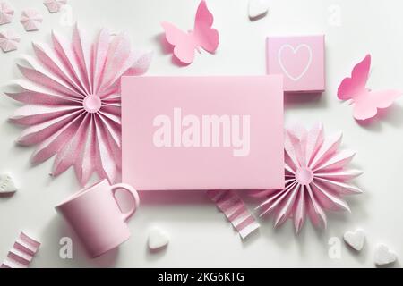 Paper fans, butterflies, flowers, espresso coffee cup. Monochromatic flat lay in baby pink on off white background. Deco frame around blank greeting Stock Photo
