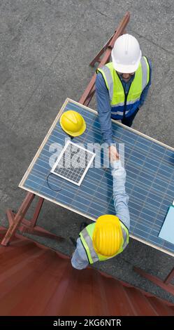 Young engineer in hardhat and safety vest shake hands with project manager after agreeing a business plan. They use solar cell panel as a table. A lar Stock Photo