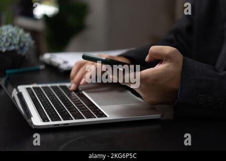 Man with mobile smartphone in his hands and using keyboard laptop. Modern digital technology concept.Freelancer at work.Working from home. Stock Photo