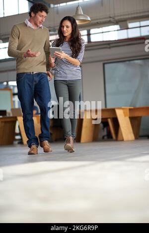 Quick update between meetings. Colleagues walking together and discussing something they are looking at on a digital tablet. Stock Photo