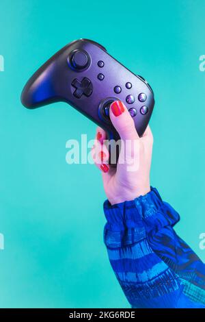 Female hand holding a video game controller gamepad isolated on a blue background studio. Stock Photo