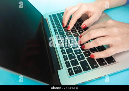 Woman hands close up using laptop with black display on blue background. Modern workspace concept. Stock Photo