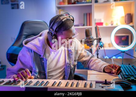 Black man artist recording music while playing electronic piano at home studio. Stock Photo