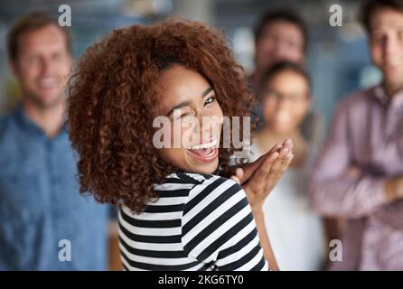 Shes the life of the office. Young woman smiling cheekily at the camera with colleagues in the background. Stock Photo