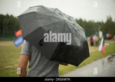 Black umbrella in rain. Large umbrella in bad weather. Man on street on cloudy day. Details of walk. Stock Photo