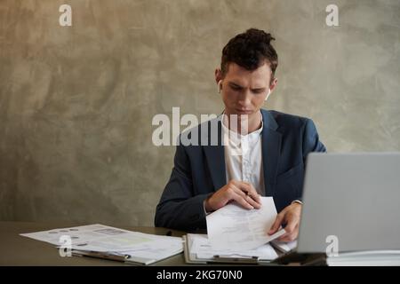 Frowning young entrepreneur working with documents at office desk Stock Photo