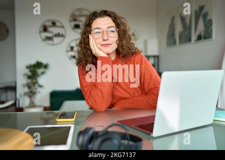 Young woman looking away and thinking while working on laptop computer at home. Stock Photo