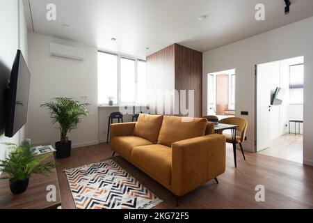 Modern living room, white wall with a TV, light orange sofa and chairs. home decoration, brown laminate, table Stock Photo