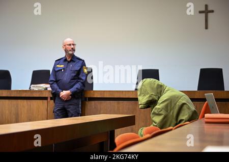 Munich, Germany. 22nd Nov, 2022. The defendant sits in his seat in the courtroom, hiding his face behind his hood while a police officer stands with him. The 85-year-old defendant has to answer for manslaughter of his dependent wife. Credit: Tobias Hase/dpa/Alamy Live News Stock Photo