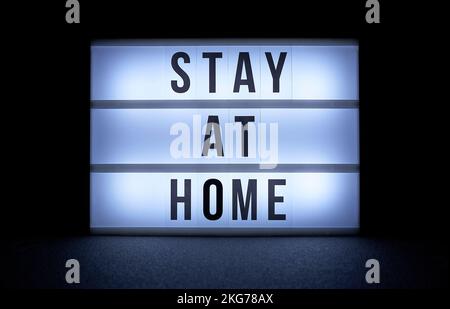 A lightbox displaying the message STAY AT HOME, black letters, illuminated against a dark background. The message is central to the image. Stock Photo